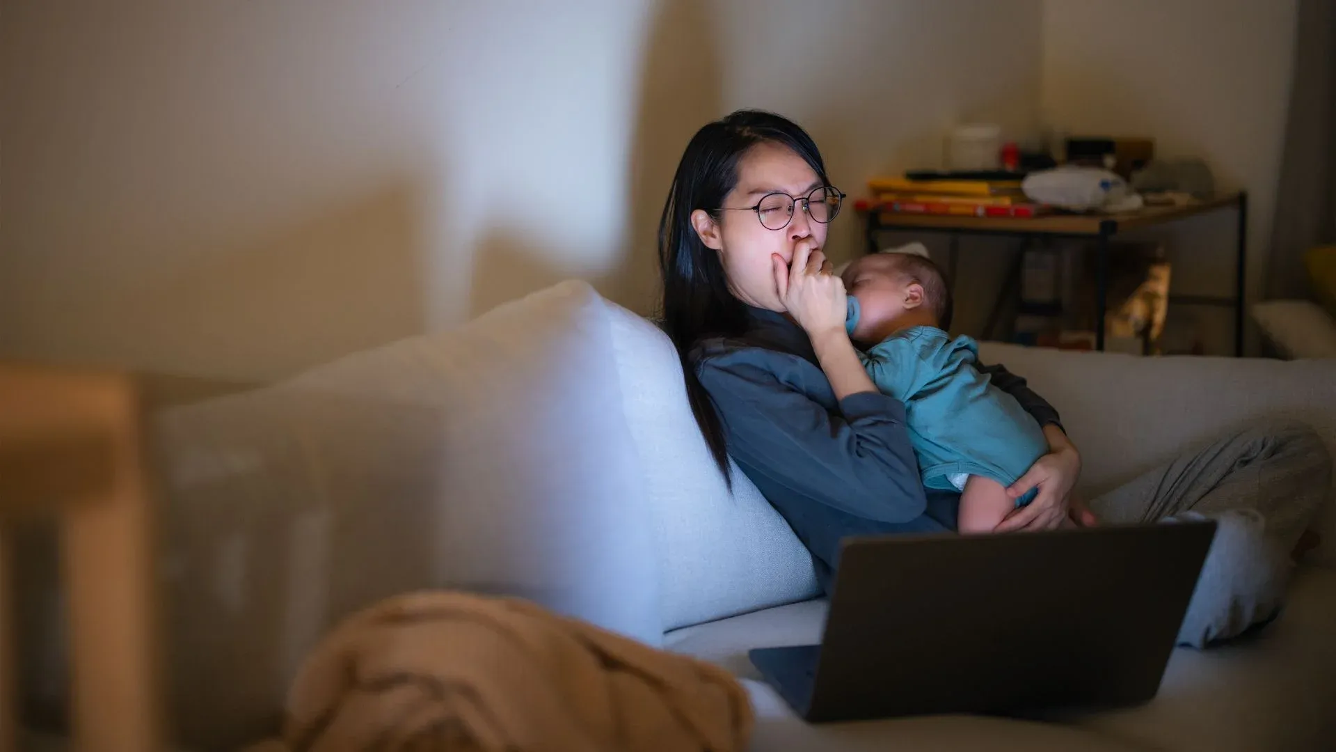 Sleep deprived mom up late with baby on the couch sleeping